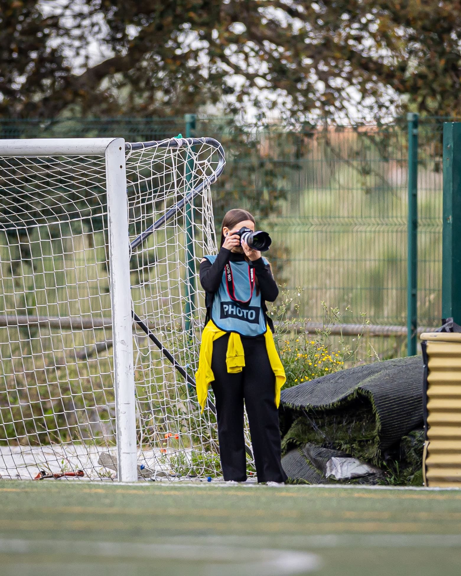Bruna a fotografar junto à baliza de um campo de futebol