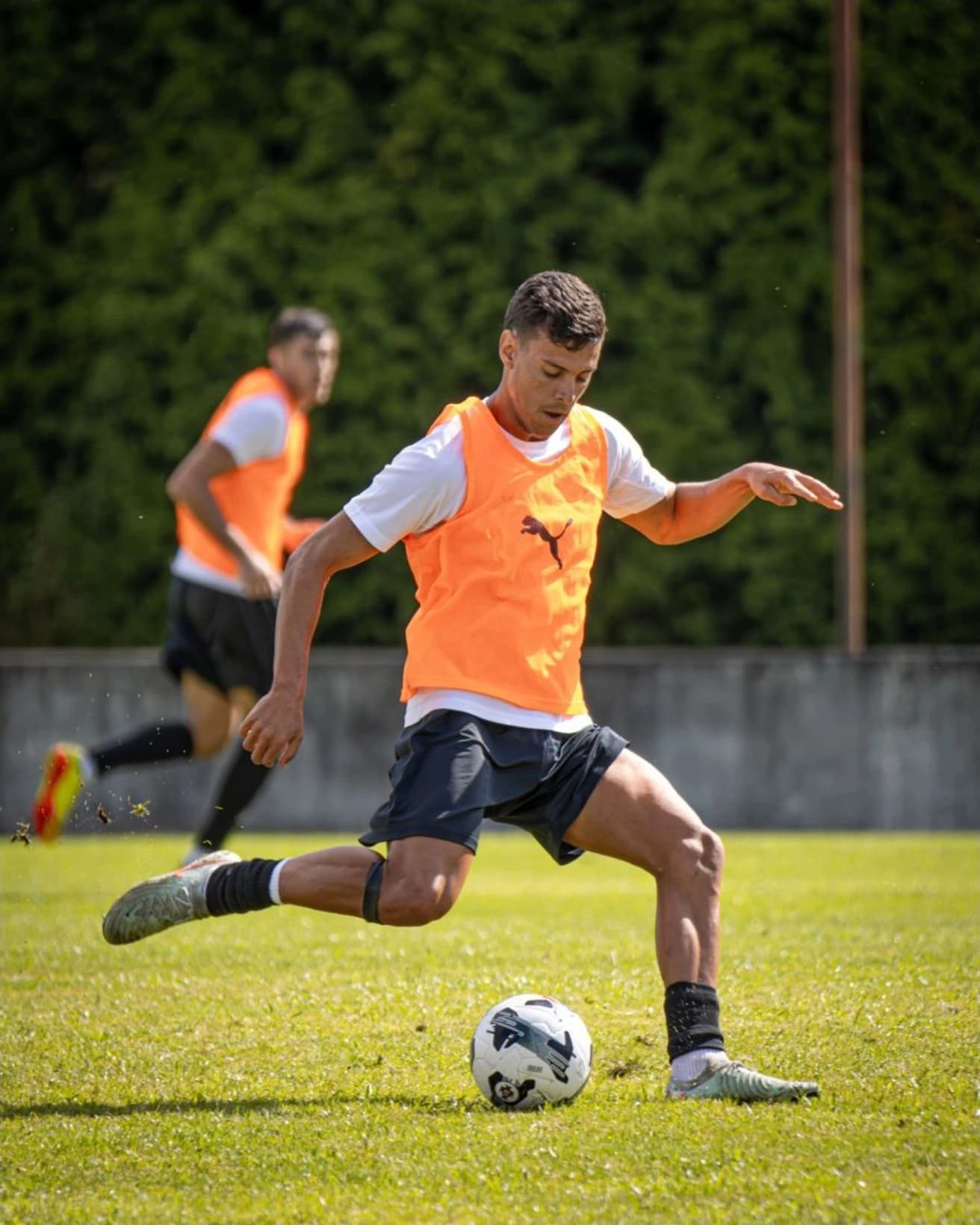 Jogador de colete laranja a rematar no treino